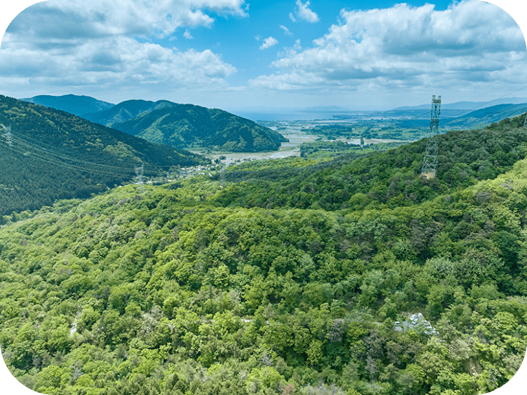 山の斜面に電波塔が建っている風景。青空には白い雲がかかっています。