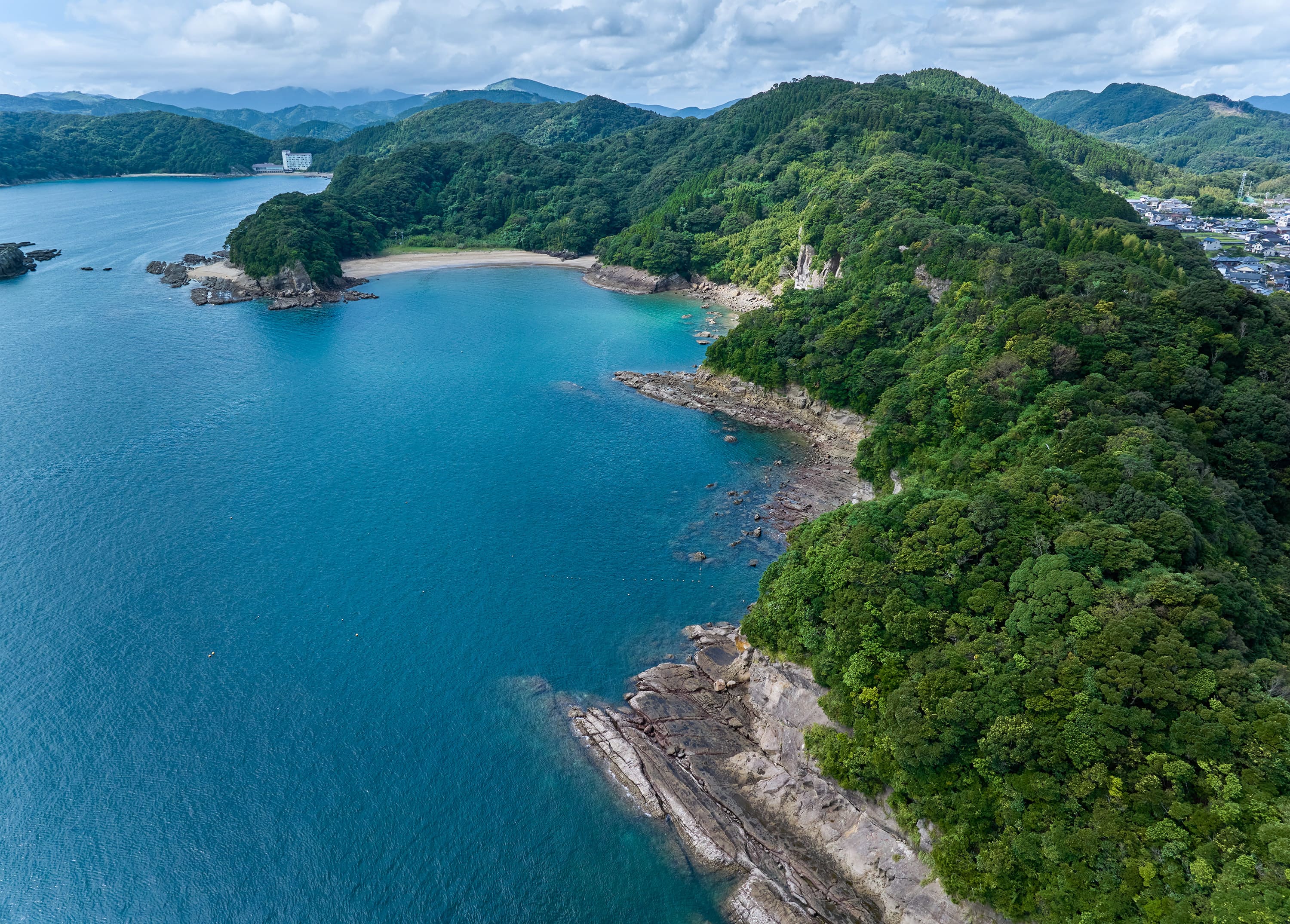 上空から見た青い海。山に囲まれており、波打ち際に岩場が見えます。