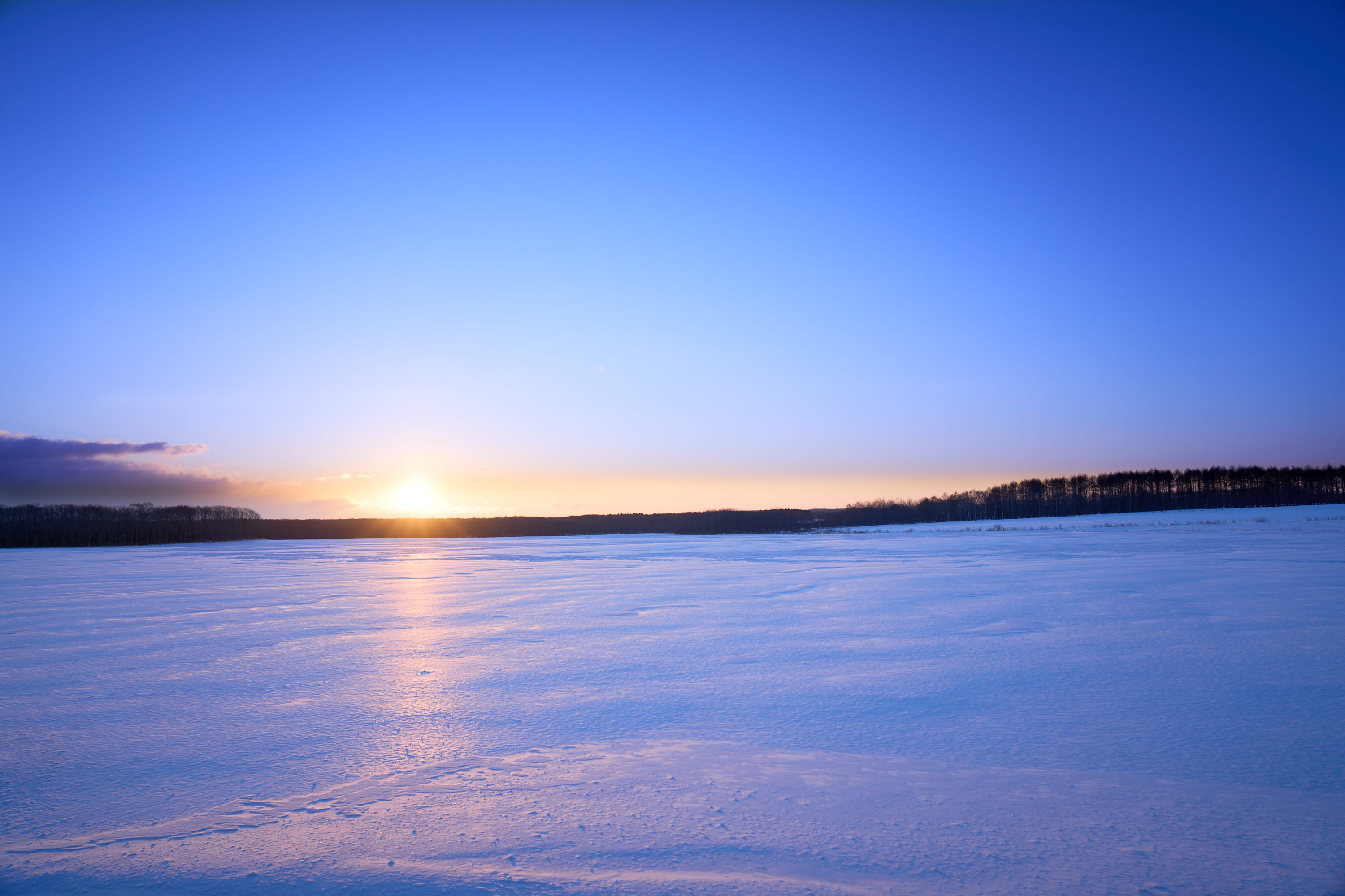 広大な広場に降り積もった雪、奥には沈みかけた夕日が見えます。